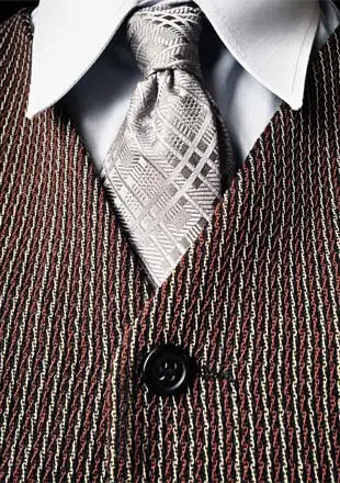 A white dress shirt adorned with a grey, plaid tie and brown vest.