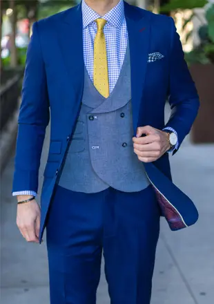 A person walks down the street wearing a royal blue tailored suit, a blue-grey vest, and a bright yellow tie.